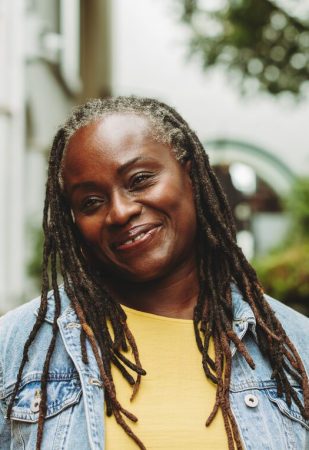 Woman with dreadlocks smiling happily while standing outdoors. Cheerful senior woman going out in casual clothing.
